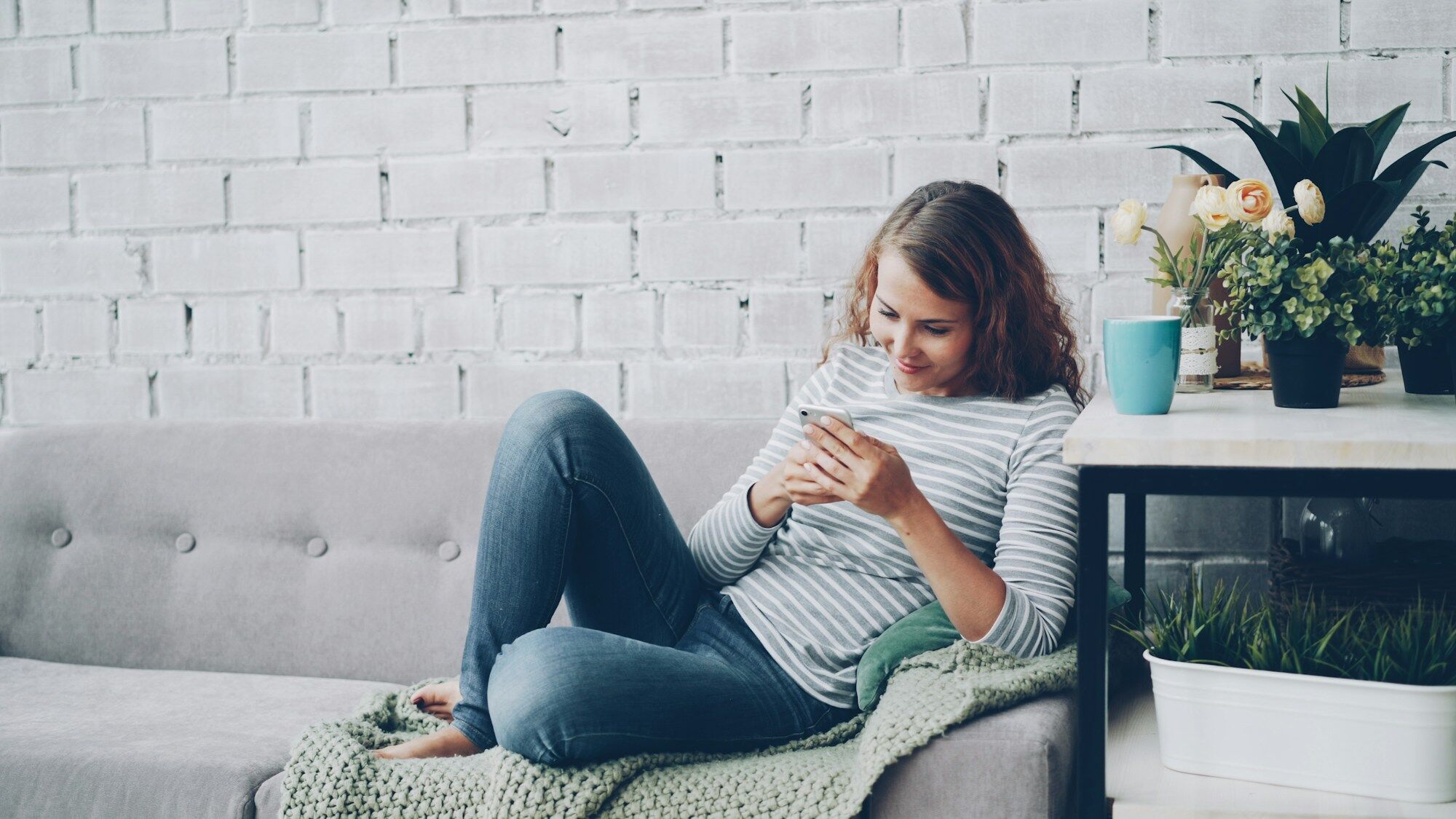 A young woman sitting on a sofa, checking her phone
